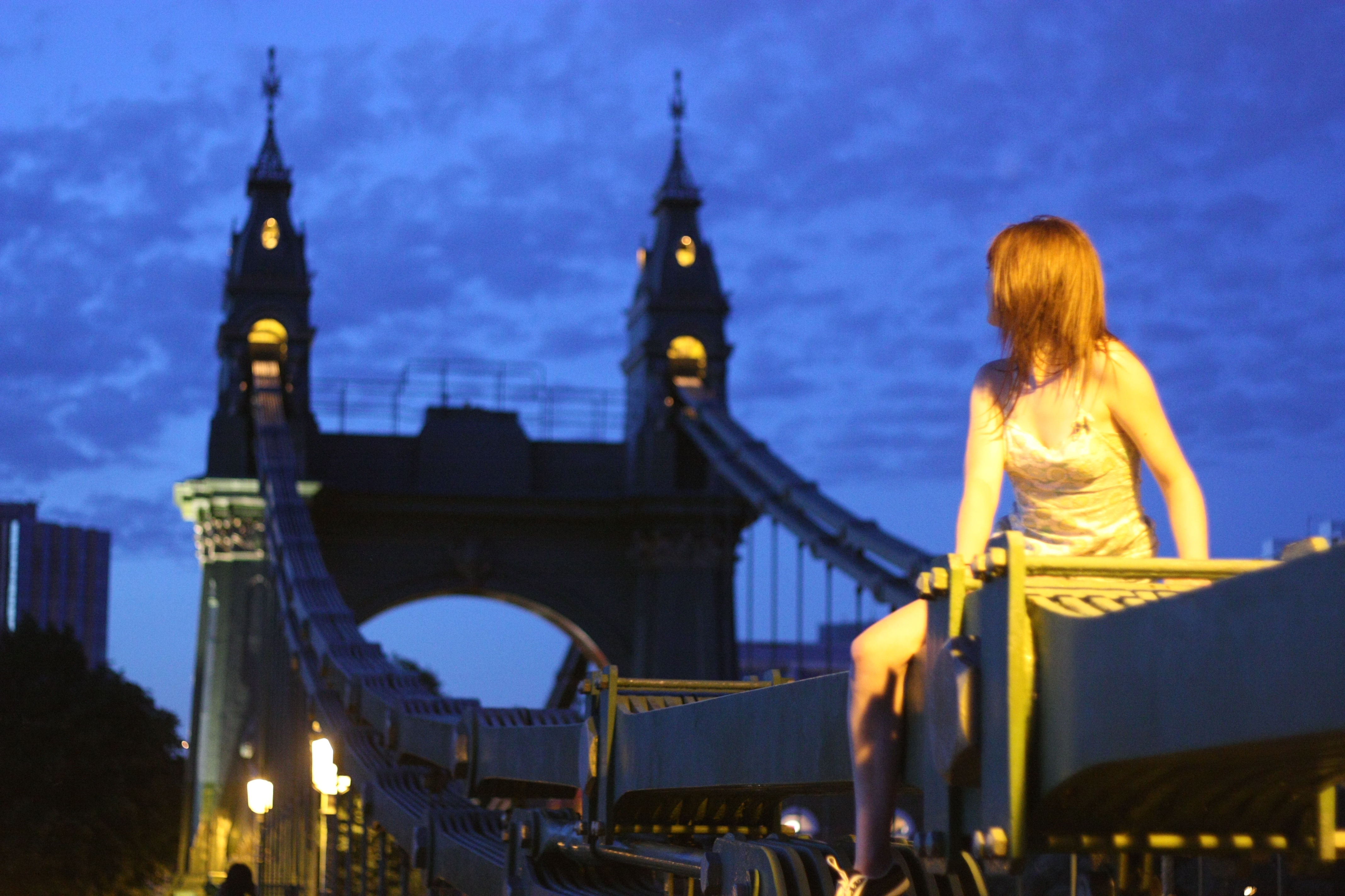 a woman sitting on a bench in front of a bridge