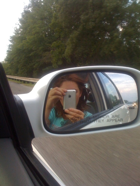 a woman taking a picture of herself in the side mirror of a car