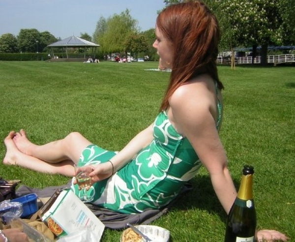 a woman sitting on the grass eating food aM har TEE