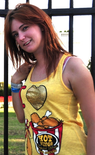 a woman in a yellow shirt is standing by a fence