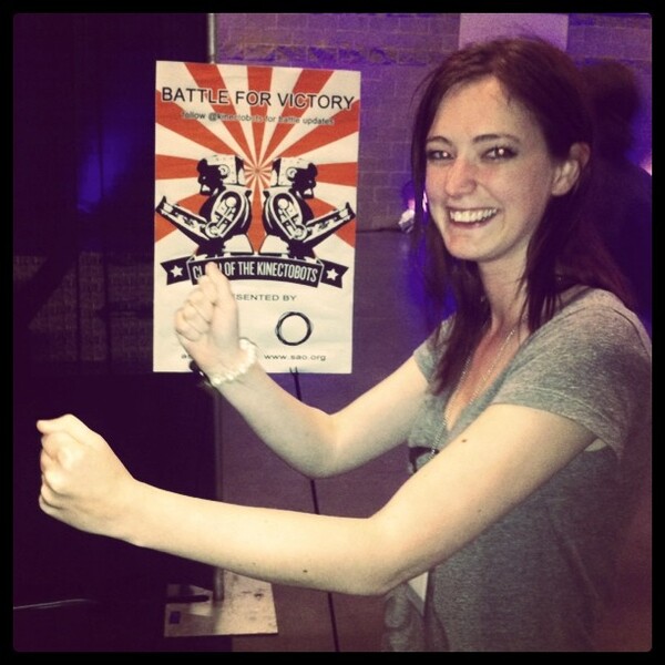 a woman holding up a poster in front of a brick wall