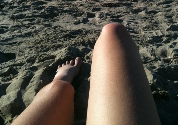 a person laying on the beach with their feet in the sand