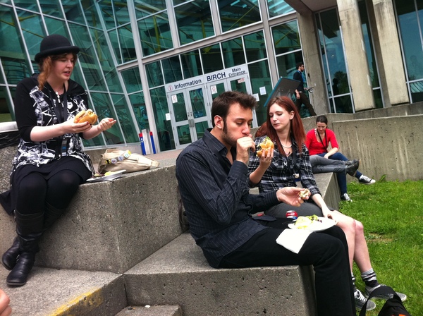 a man and woman sitting on a concrete bench eating food