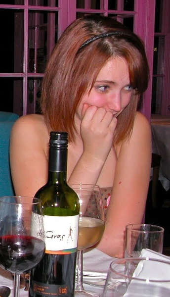 a woman sitting at a table with a bottle of wine