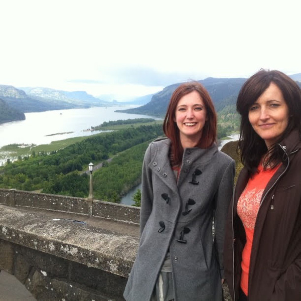 two women standing on a wall overlooking a lake