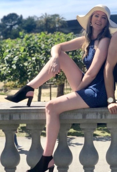 a woman in a blue dress and hat sitting on a stone wall