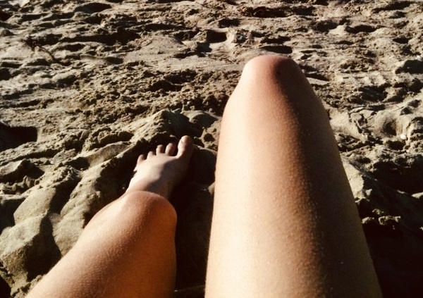 a person laying on the beach with their feet in the sand