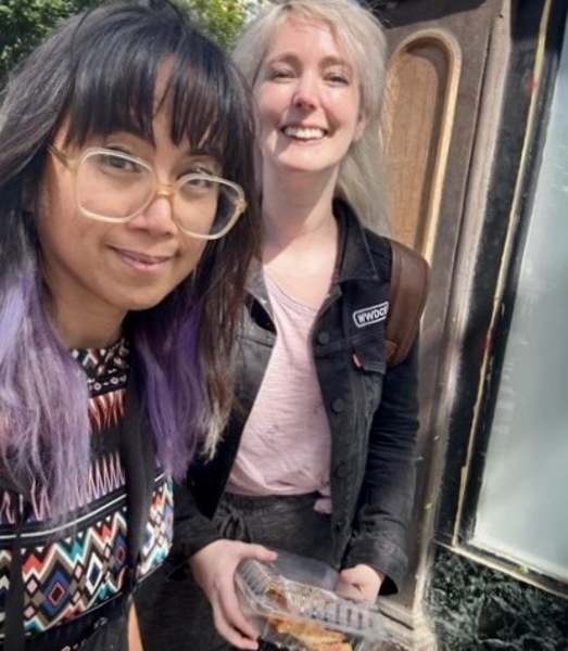 two women standing next to a van with a sign