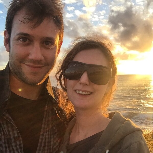 a man and woman standing on the beach at sunset