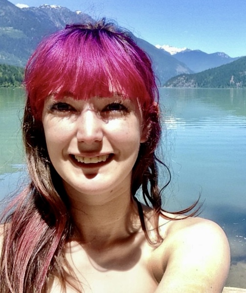 a woman with pink hair standing in front of a lake