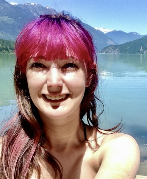 a woman with pink hair standing in front of a lake