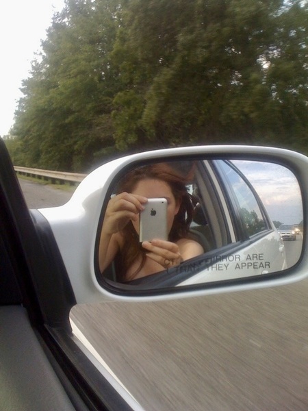 a woman taking a picture of herself in the side mirror of a car