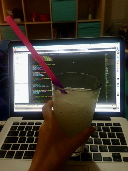 a person holding a drink in front of a laptop