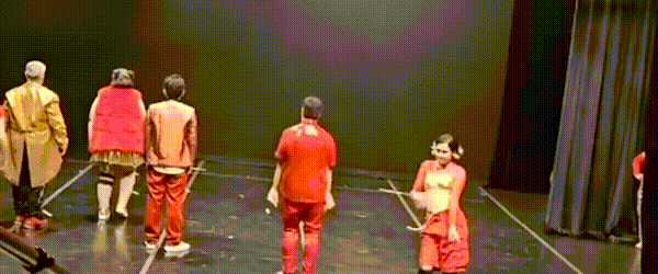 a group of people standing on a stage 
a group of people on stage with one person in the middle 
a group of people on stage with one person in red shirt 
a group of people on stage with arms in the air 
a group of women in red shirts dancing on stage 

 YOU FUCKER