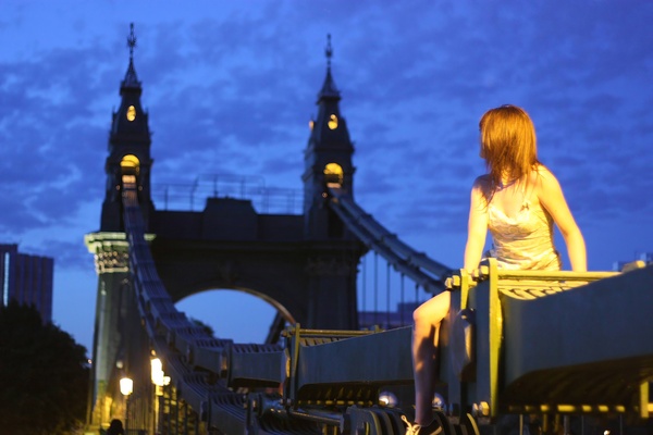 a woman sitting on a bench in front of a bridge sie
o wer,
AN