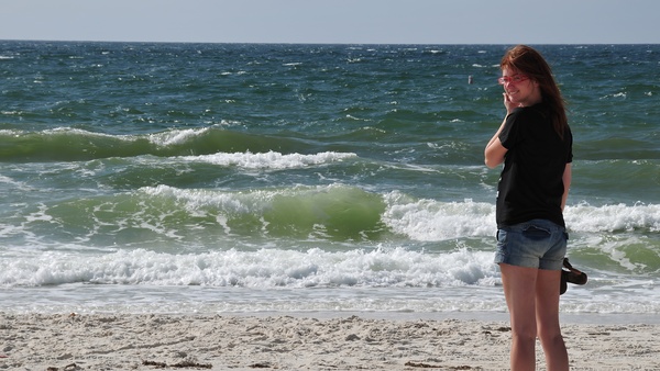 a woman standing on the beach with a cellphone in her hand