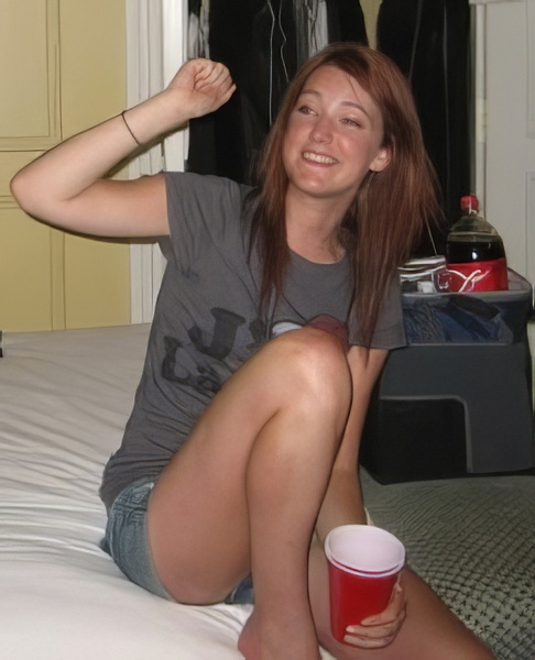 a woman sitting on a bed with a cup of beer