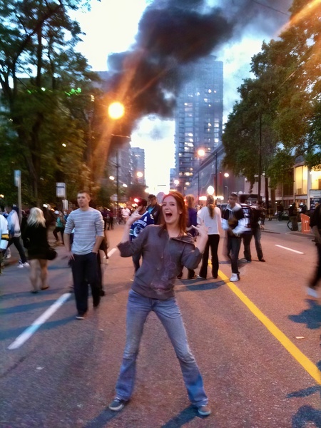 a woman is running in the street with a fire in the background