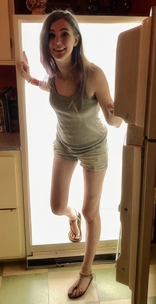 a woman in a gray shirt and shorts is standing in a kitchen