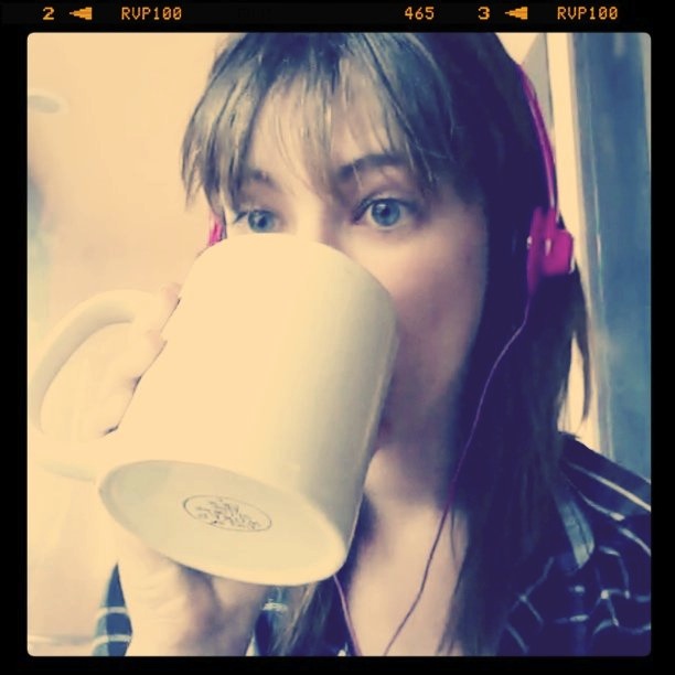 a woman drinking from a cup while wearing headphones