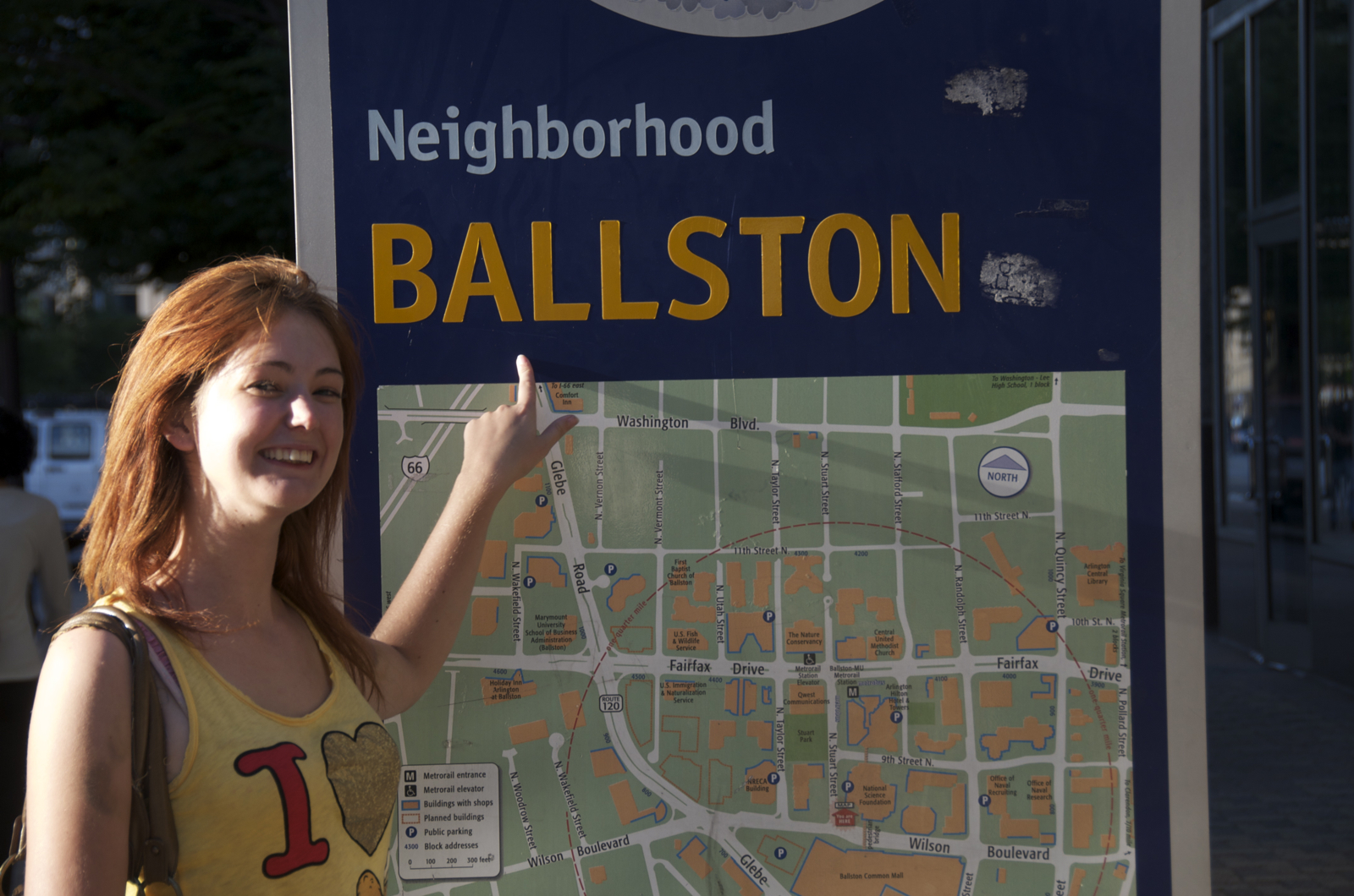 a woman pointing at a sign ——_— a
Neighborhood

Washington
Fairfax
e
Wihan
Boulevard