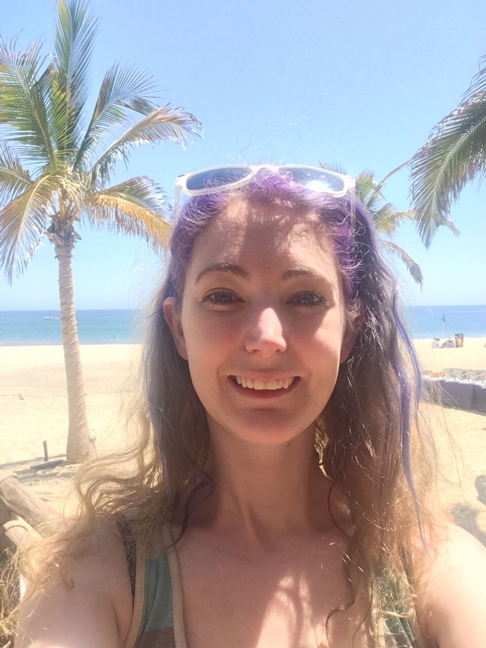 a woman with purple hair and sunglasses on the beach