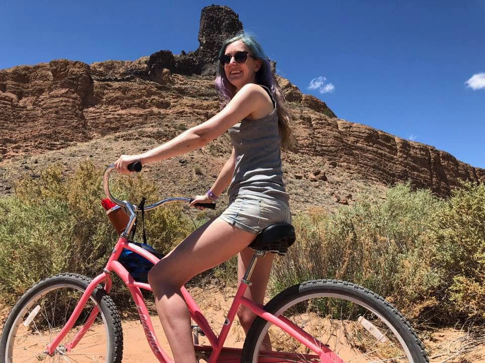 a woman riding a pink bike on a dirt road