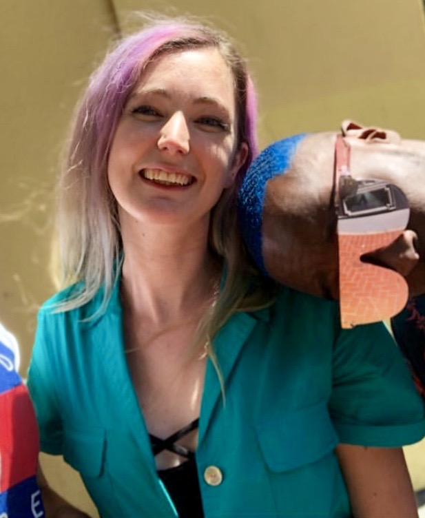 a woman in a green jacket and blue shirt holding a small dog