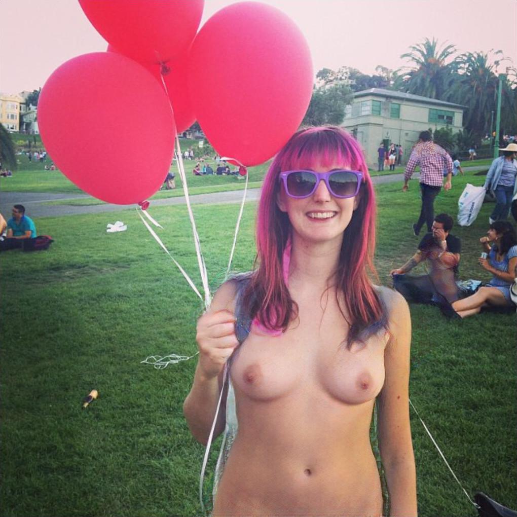 a woman with pink hair and sunglasses holding red balloons