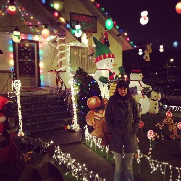 a man and woman standing in front of a house decorated with christmas lights