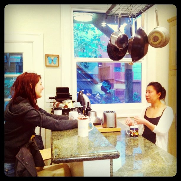 a woman sitting at a kitchen counter with a pot hanging from the ceiling