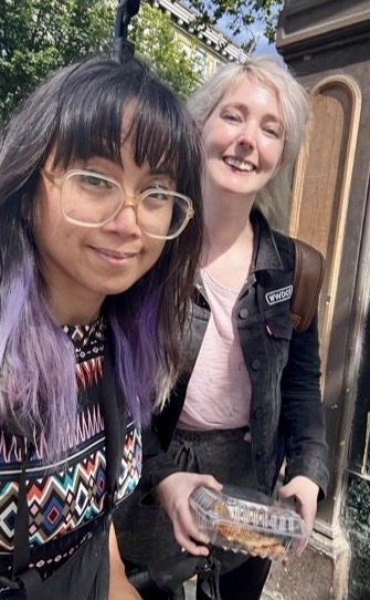 two women are standing outside with a small box