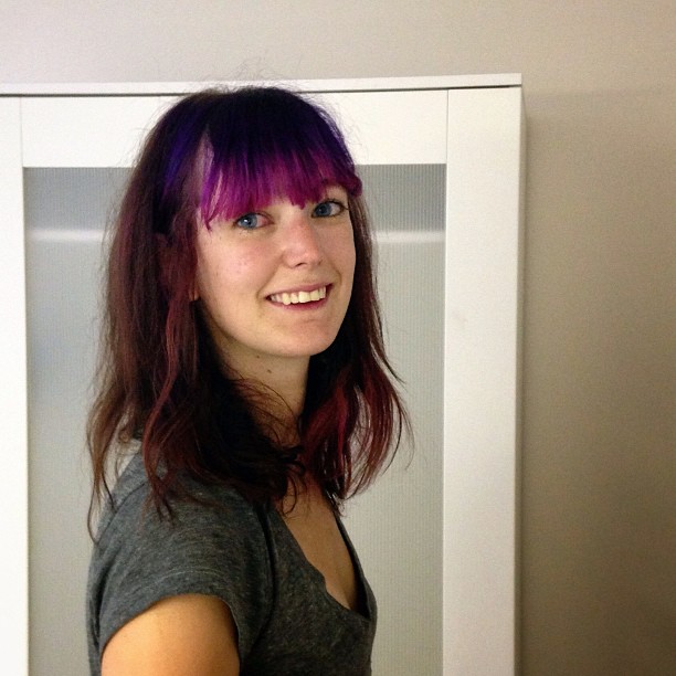 a woman with purple hair standing in front of a mirror