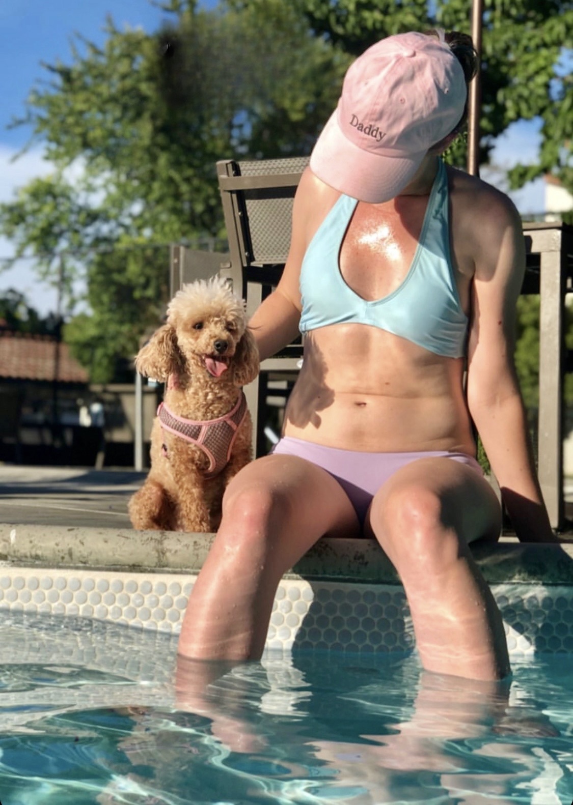 a woman in a bikini and hat sitting in a pool with her dog