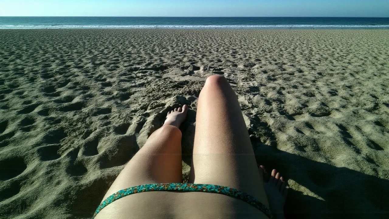 a person laying on the beach with their feet in the sand