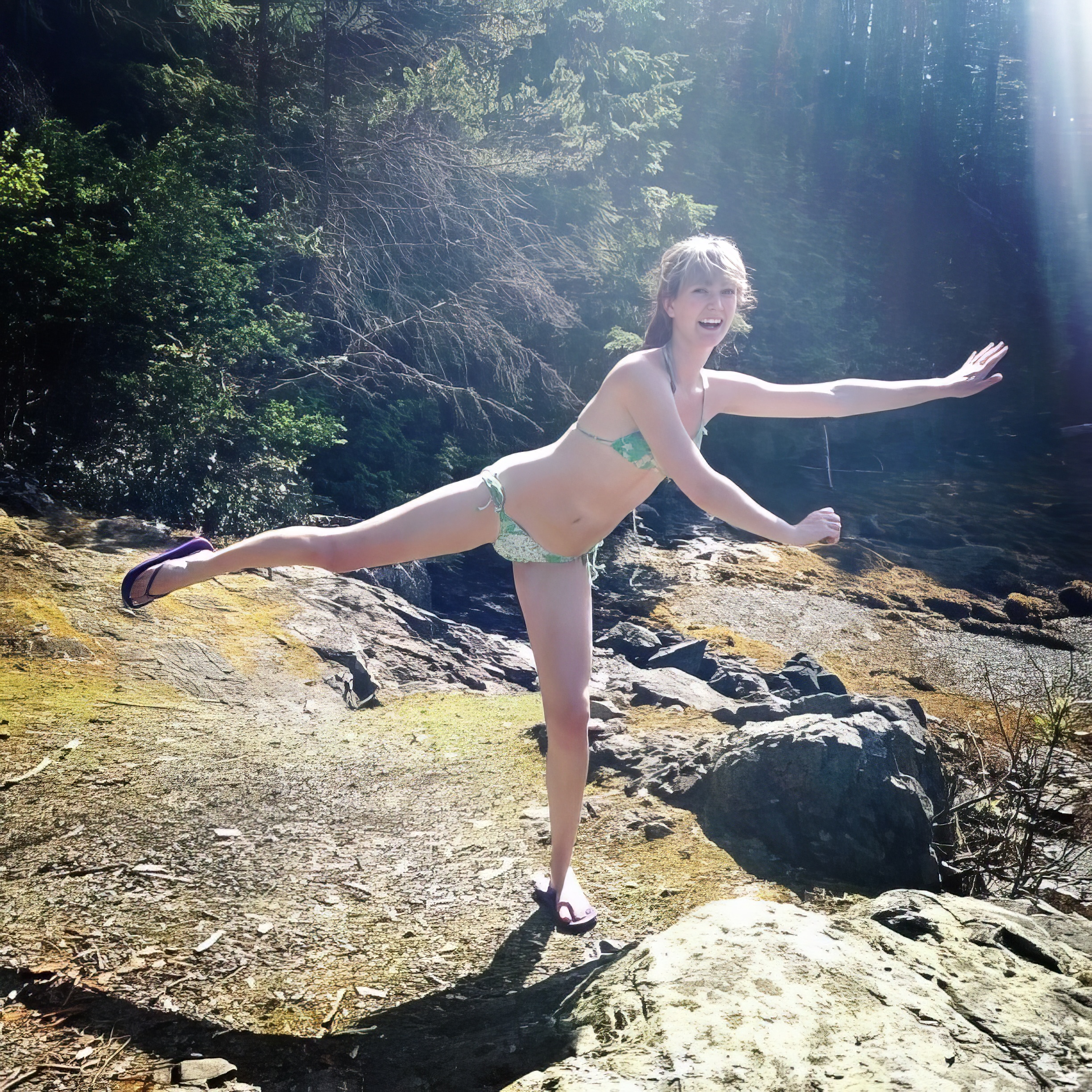 a woman in a bikini is standing on a rock