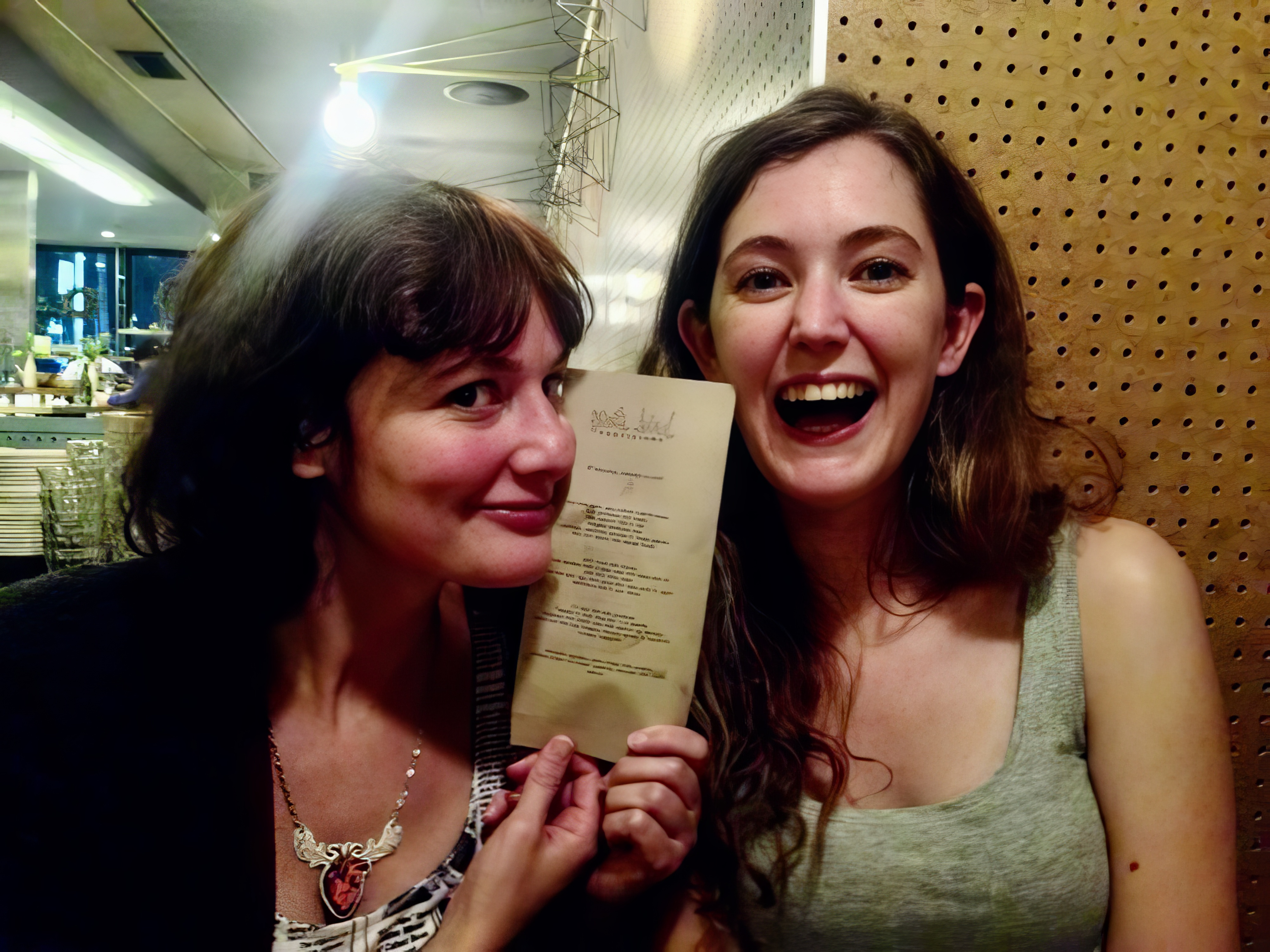 two women are smiling and holding a menu