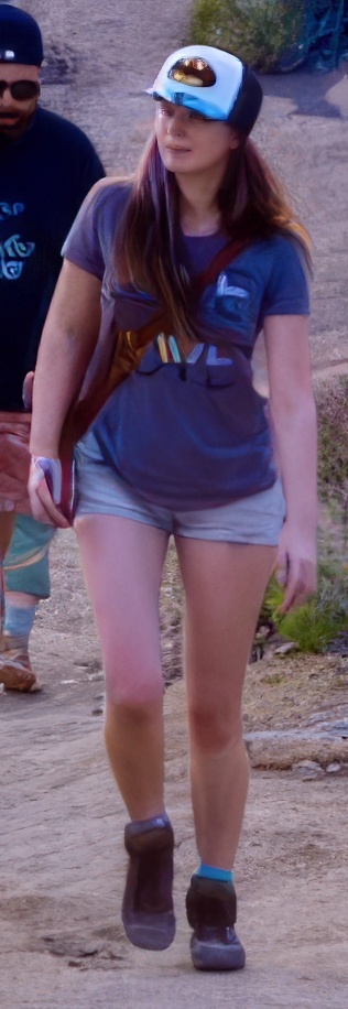 a woman walking down a dirt road with a man behind her